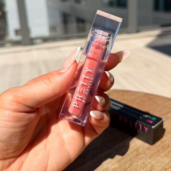 Hand holding a lip gloss with 'Pretty' text against a cityscape background