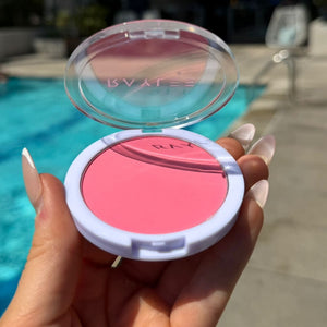 Hand holding a pink makeup compact with a blurred outdoor background