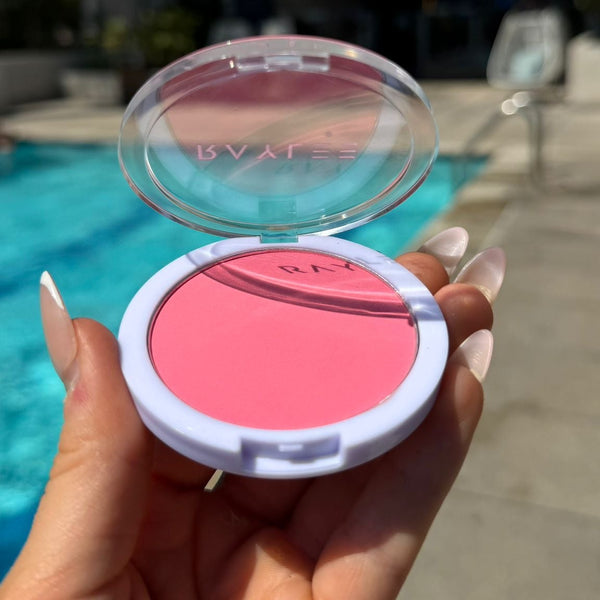 Hand holding a pink makeup compact with a blurred outdoor background
